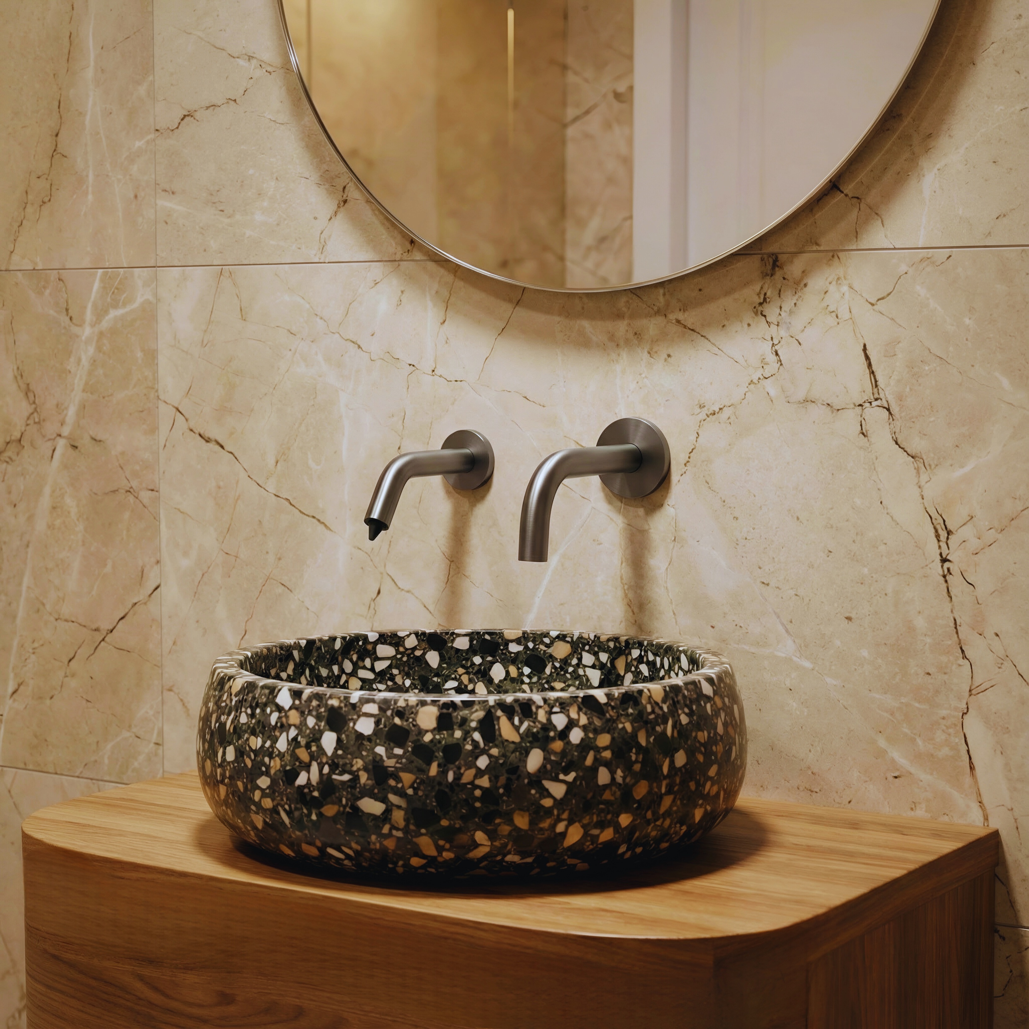 Brushed nickel wall-mounted faucet model installed above a black terrazzo vessel sink on a wood vanity with marble wall tile and round mirror.